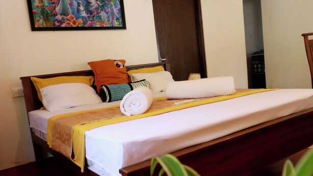 A neatly made bed with a white and yellow bedspread, a rolled white towel, and a variety of pillows including a cartoon character pillow. - Nature Beat Villa – Exclusive Tropical Retreat Near Mirissa (kamburugamuwa)