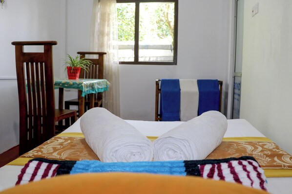 A room with a bed, a table with a plant, and a window.