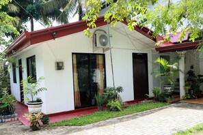 A two-story building with a red roof, large windows, and a small porch area with potted plants.