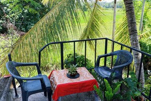 A table with a red tablecloth and a potted plant, two chairs, and a metal railing.