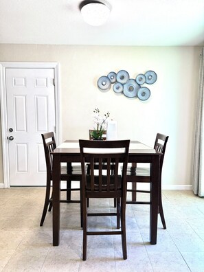 A dining area with a white door, a ceiling light, a wall-mounted decorative plate, and a table with chairs.