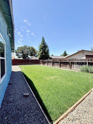 A backyard with a well-maintained lawn, a wooden fence, and a house in the background.