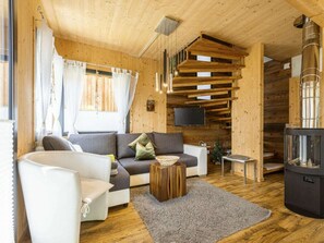 A cozy cabin interior with a sofa, a white chair, a small wooden table, a fireplace, and a TV mounted on the wall. - Cabin With 1 Bedroom (Sankt Georgen am Kreischberg)