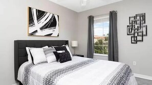 A modern bedroom with a large bed, a bedside table, a lamp, and a window with curtains.
