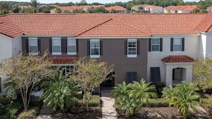 A multi-story residential building with a red-tiled roof, multiple windows, and a small covered entrance.