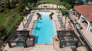 A swimming pool with sun loungers and a covered seating area, surrounded by a fence and greenery.