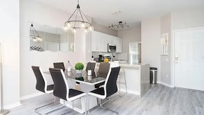 A modern kitchen with white cabinets, a central island, and a dining area with a glass table and black chairs.