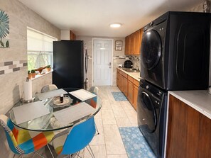 A compact kitchen with a glass dining table, a black refrigerator, a washing machine, and wooden cabinets. - Cozy Private Studio.  Parking & Fenced Yard (Jacksonville)
