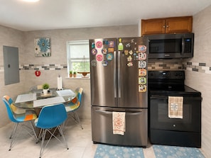 A modern kitchen with a stainless steel refrigerator, a microwave, and a dishwasher. There is a dining table with colorful chairs and a window with plants. - Cozy Private Studio.  Parking & Fenced Yard (Jacksonville)
