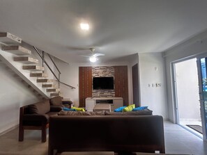 A modern living room with a staircase, a flat-screen TV, and a ceiling fan. - CJ17AR/3D-Paraíso em Arraial D’ajuda/Praia e Lazer (Arraial da Ajuda)