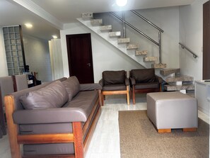 Uma sala de estar moderna com um sofá seccional, duas poltronas, uma mesa de centro, uma escada com corrimão de metal e uma porta.