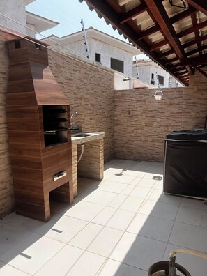 A patio area with a built-in grill, a sink, and a tiled floor. - CJ17AR/3D-Paraíso em Arraial D’ajuda/Praia e Lazer (Arraial da Ajuda)