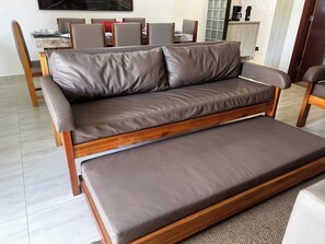 Ein modernes Wohnzimmer mit einer Couch und einem Couchtisch, eine Essecke mit Stühlen und einem Tisch sowie eine Küchenzeile mit einer Kaffeemaschine.