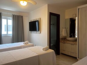 Ein Hotelzimmer mit zwei Betten, einem Fernseher, einem Badezimmer mit Waschbecken und einem Spiegel.