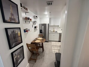 A narrow hallway leading to a kitchen with white cabinets, a stainless steel refrigerator, and a dining area with a table and chairs. - Cozy 1-bedroom apartment in wonderful Miami Beach with AC (Miami Beach)
