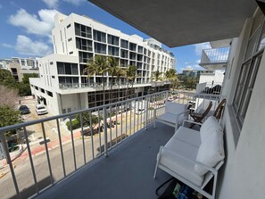 Ein Balkon mit einer weißen Couch und einem Tisch, mit Blick auf eine Straße mit Autos und Palmen.