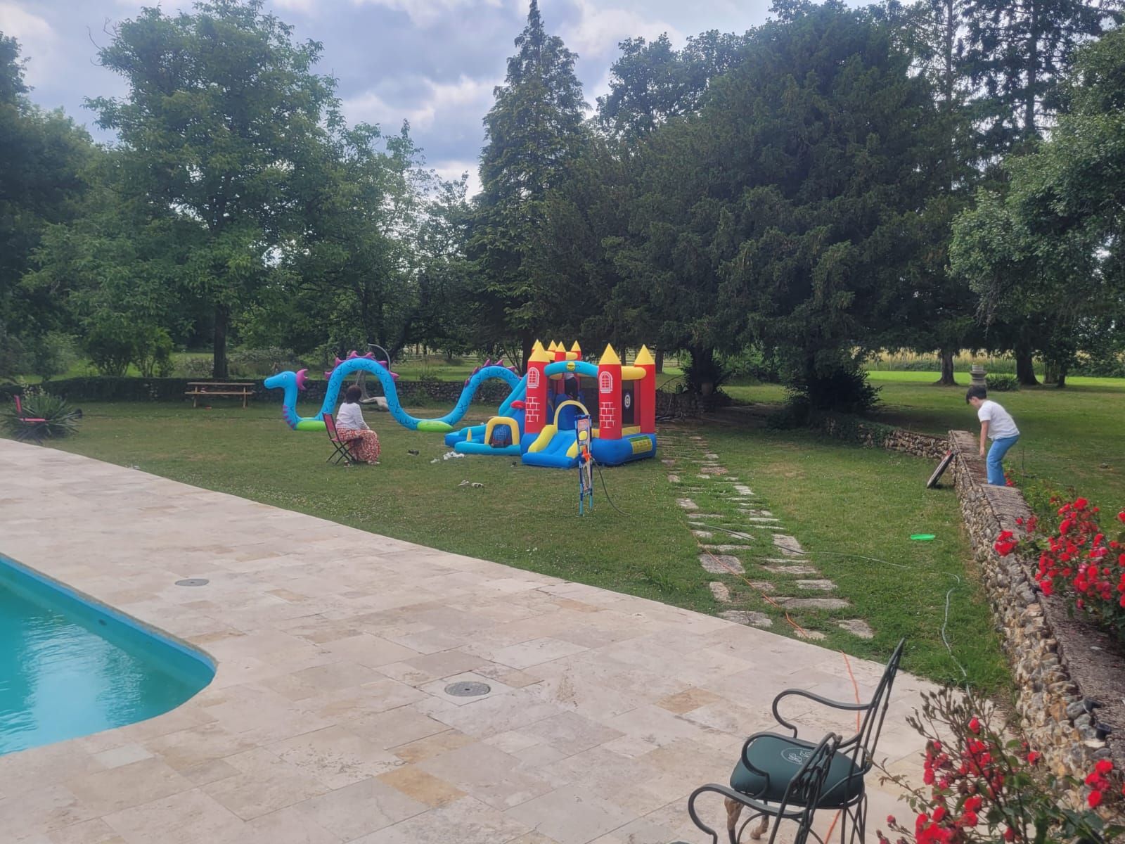 A swimming pool with a slide and a small inflatable play structure in a grassy area.