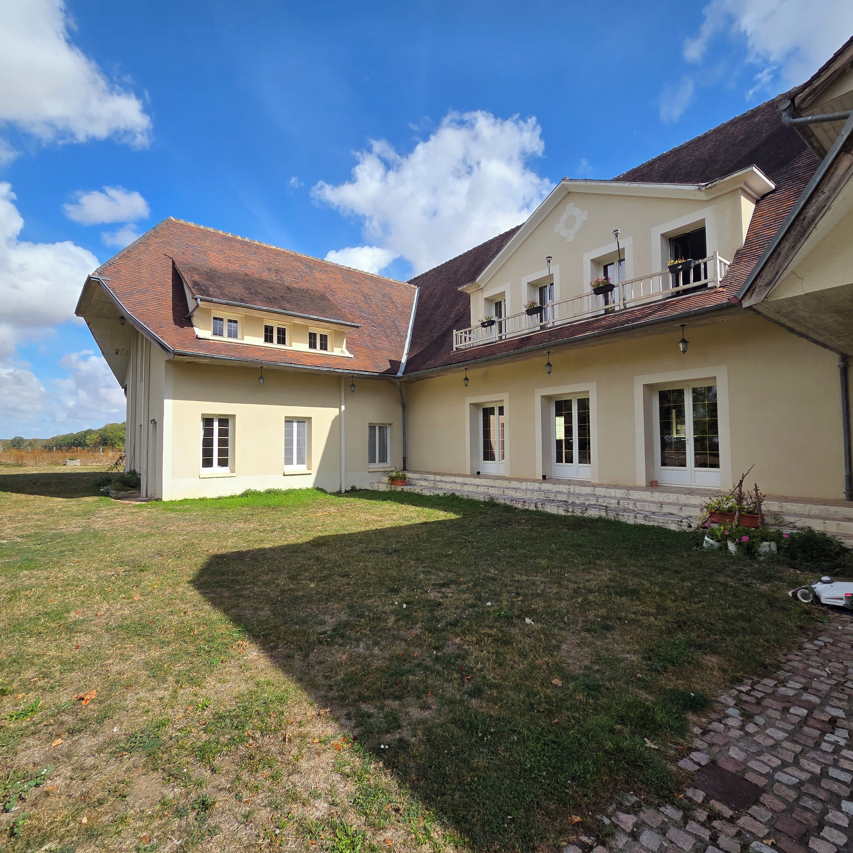 Une maison à deux étages avec un toit en pente, de nombreuses fenêtres et un petit jardin.