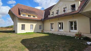 Une maison à deux étages avec un toit en pente, de nombreuses fenêtres et un petit jardin.