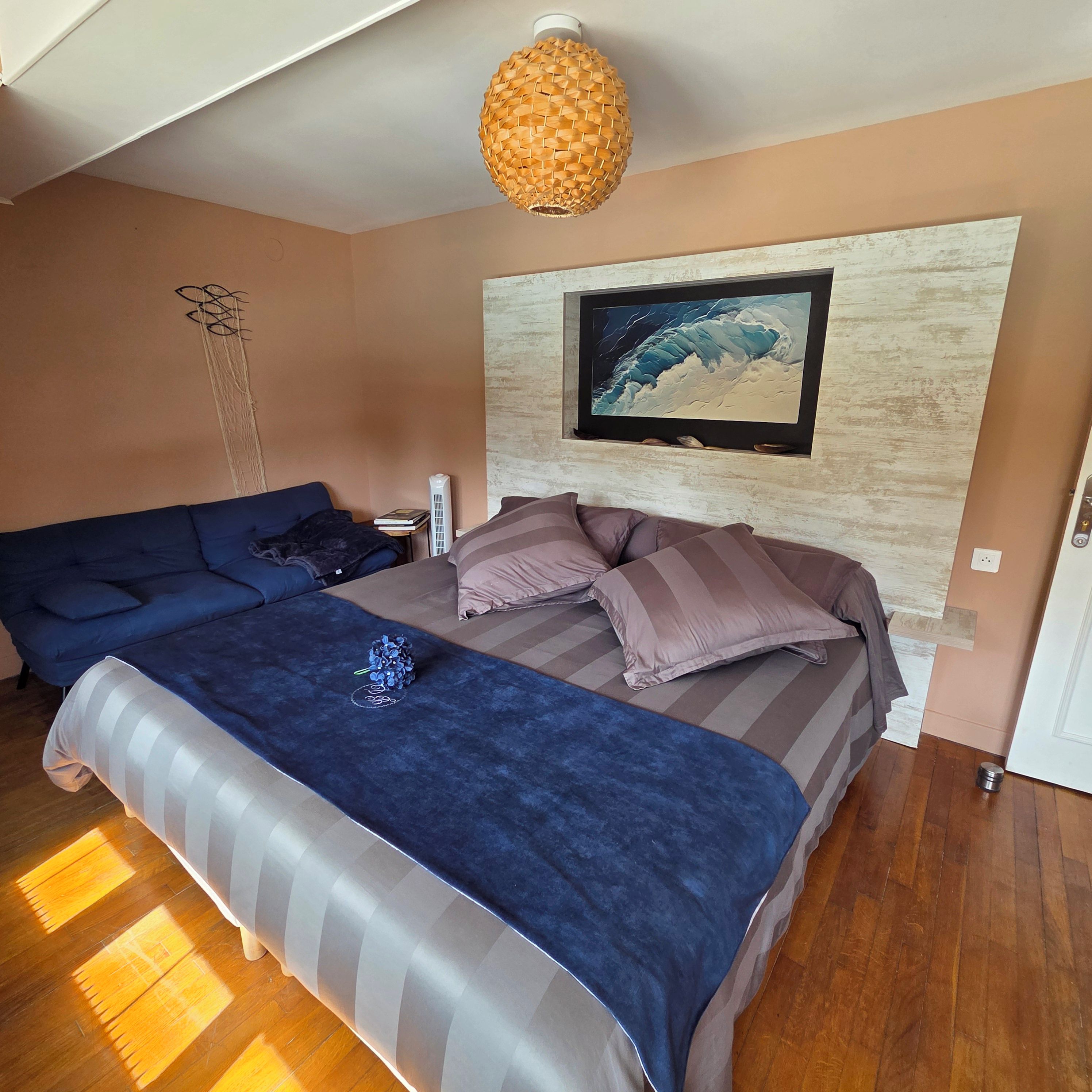 A bedroom with a bed, a sofa, a painting on the wall, and a ceiling light fixture.