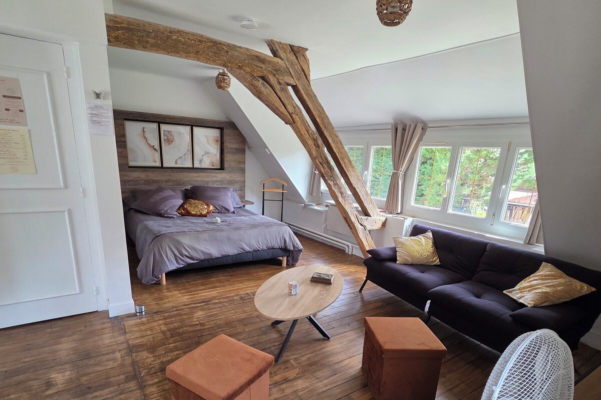 A loft-style bedroom with a sloped ceiling, a bed with a headboard, a sofa, a coffee table, and a fan.