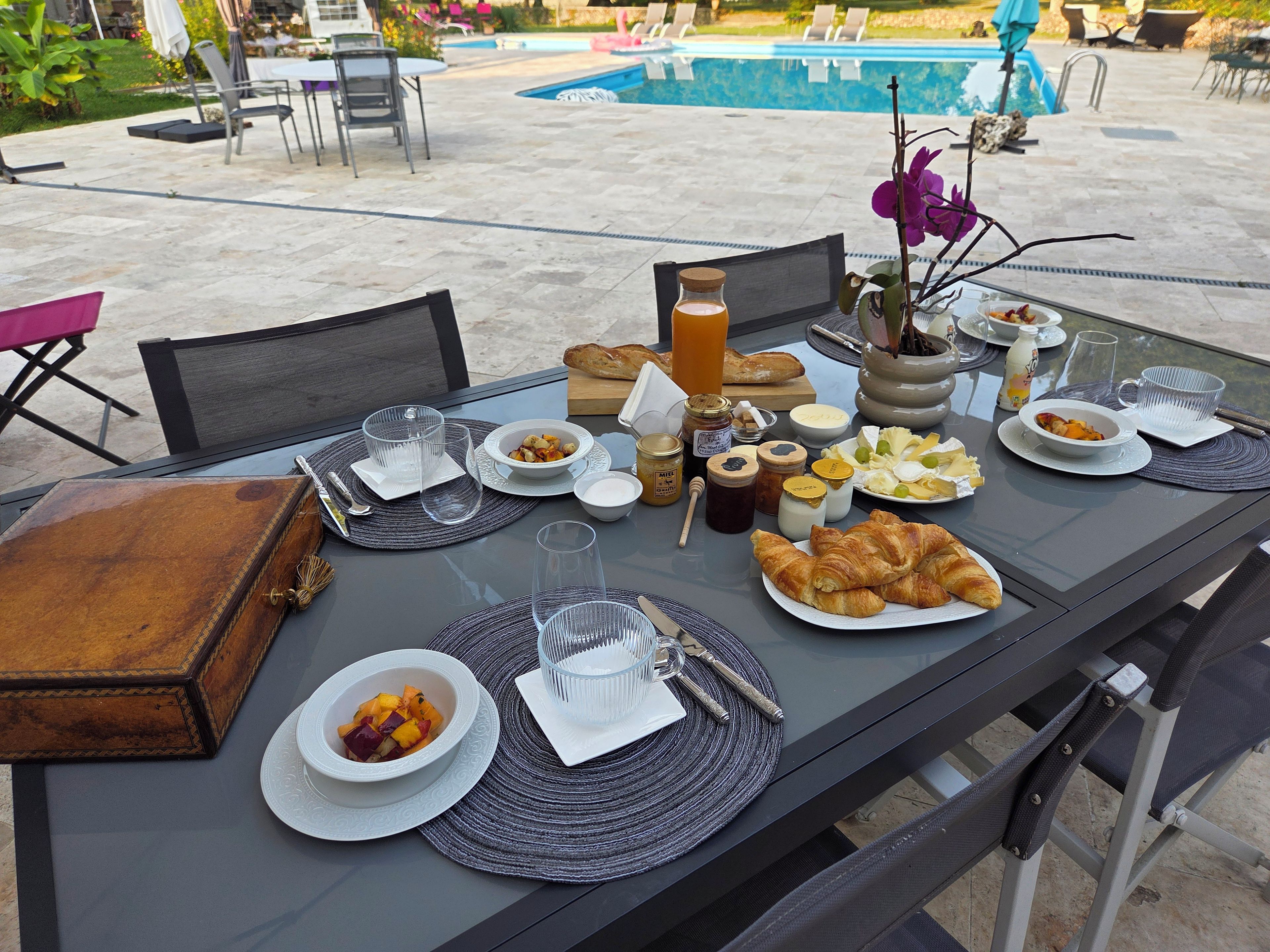 Un espacio de comedor al aire libre con una mesa preparada para el desayuno, que incluye croissants, fruta y bebidas.