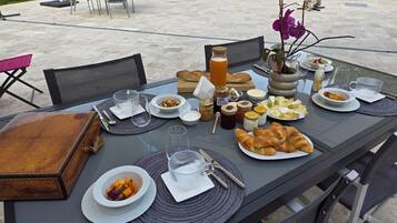 Un espacio de comedor al aire libre con una mesa preparada para el desayuno, que incluye croissants, fruta y bebidas.