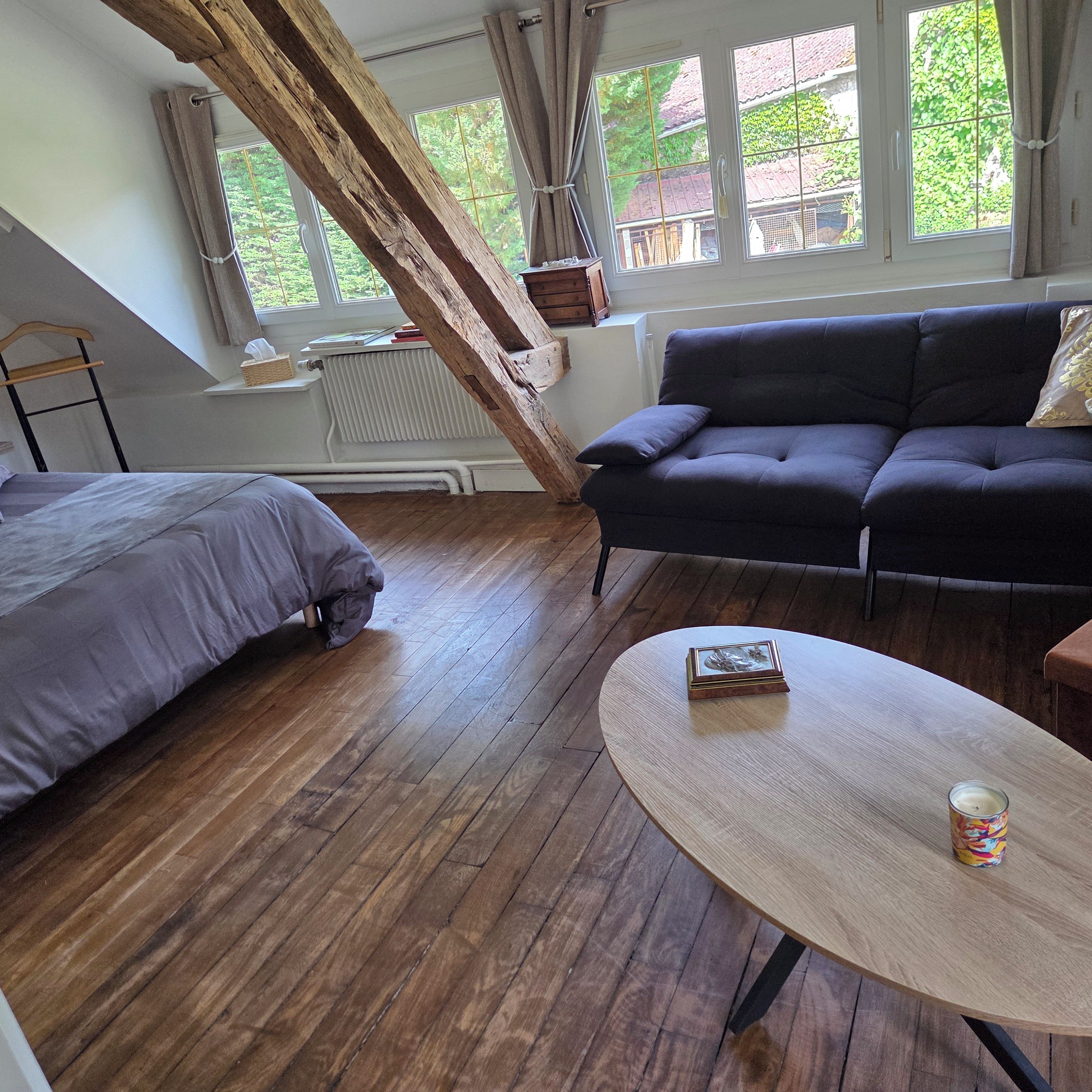 A room with a bed, a sofa, a table, and a window with a view of greenery.