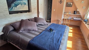 Un dormitorio con cama, un cuadro, una lámpara colgante y una mesita con hervidor.