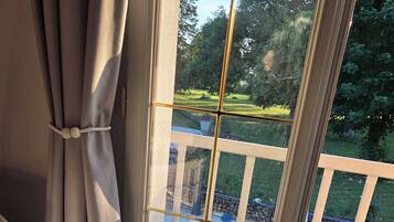 Ein Zimmer mit großem Fenster, Vorhängen und Blick auf eine Terrasse mit Stuhl und Tisch.