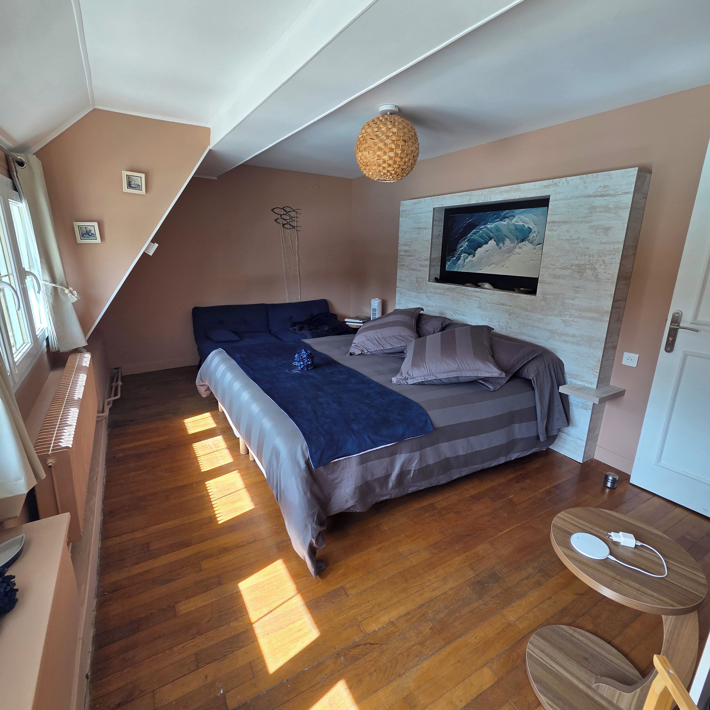 Un dormitorio con una cama, un televisor montado en la pared, una mesita y una silla.
