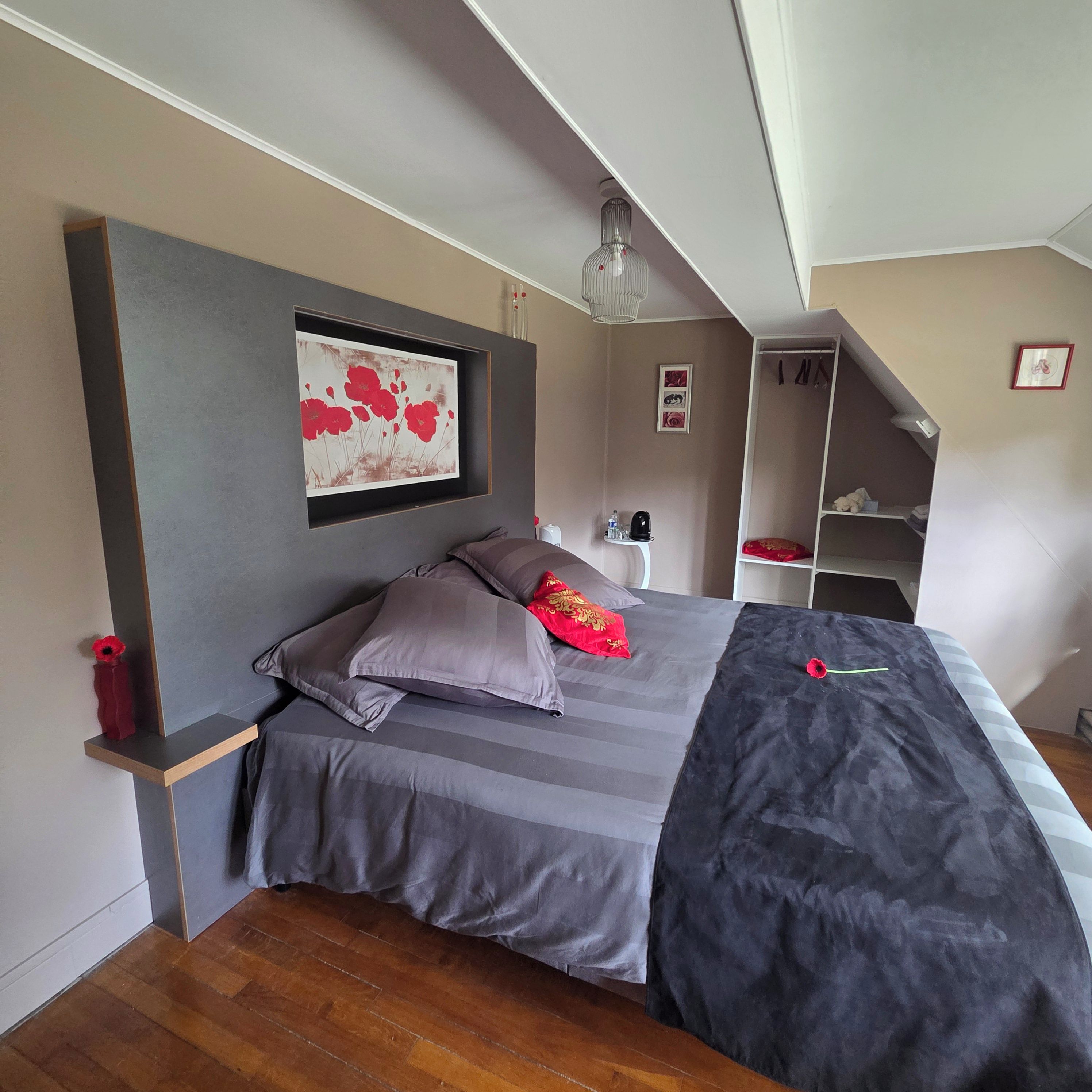 Une chambre à coucher comprenant un lit, une table de chevet, une étagère, un tableau encadré et un luminaire suspendu.