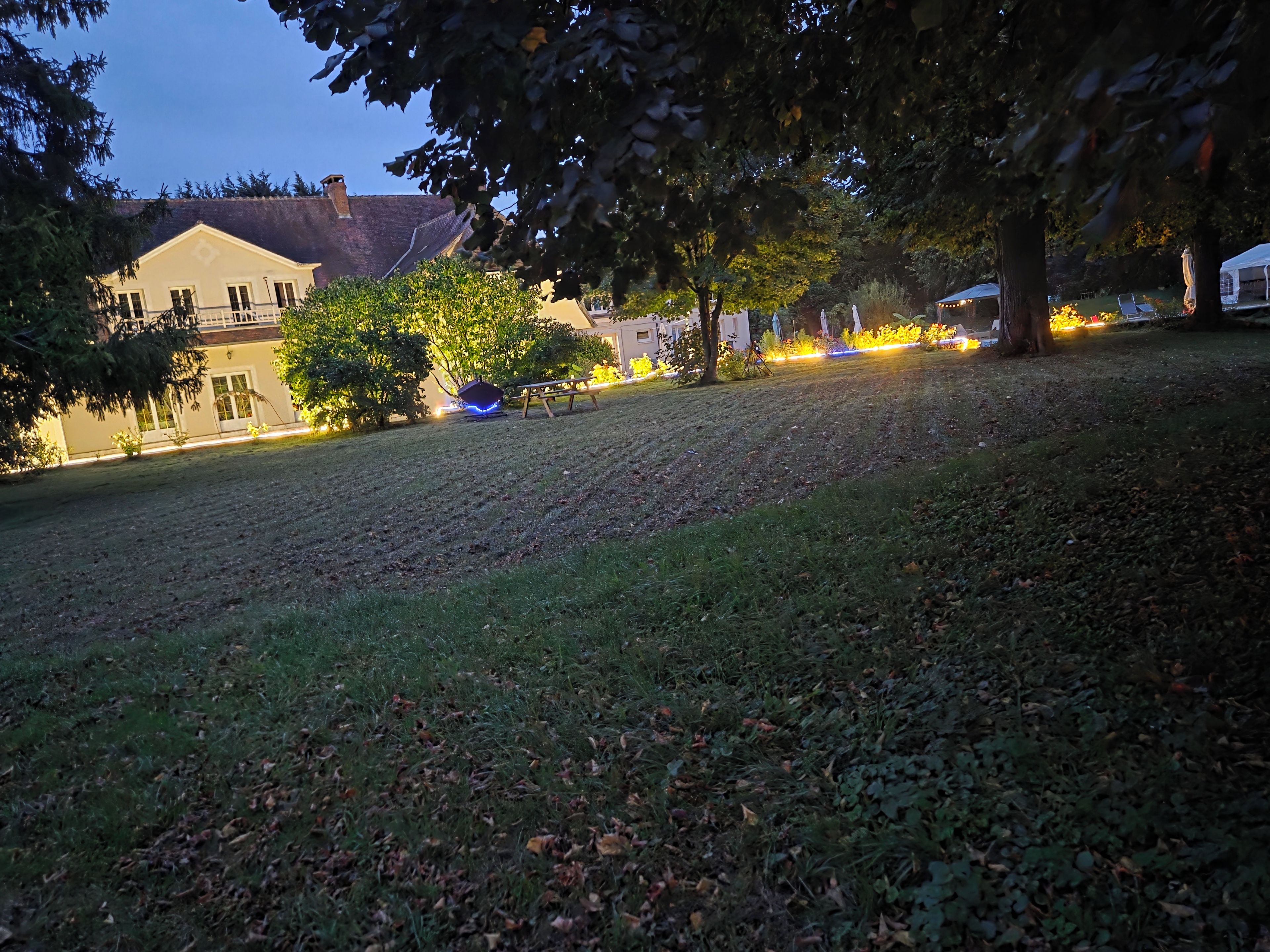 Een gazon met een grasmaaier, bomen en een gebouw op de achtergrond.