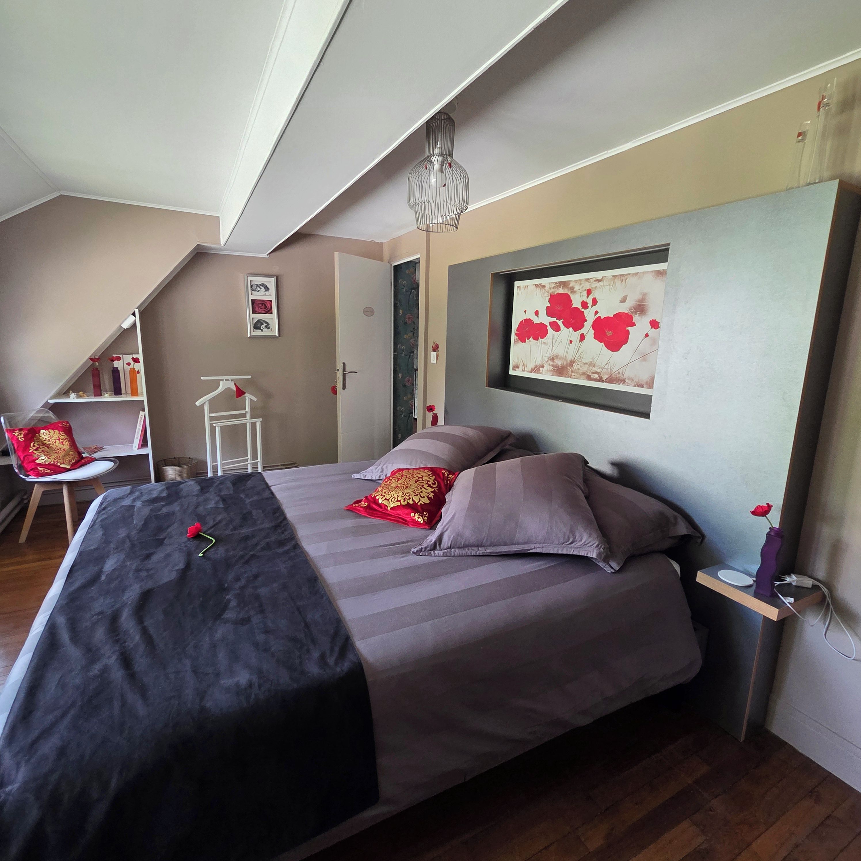A bedroom with a bed, a chair, a shelf with books, and a painting on the wall.