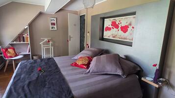 A bedroom with a bed, a chair, a shelf with books, and a painting on the wall.