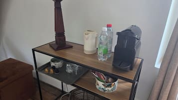 A wooden table with a lamp, water bottles, a kettle, and a basket with snacks.