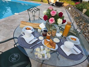 A breakfast table with croissants, fruit, and beverages, set outdoors near a pool.