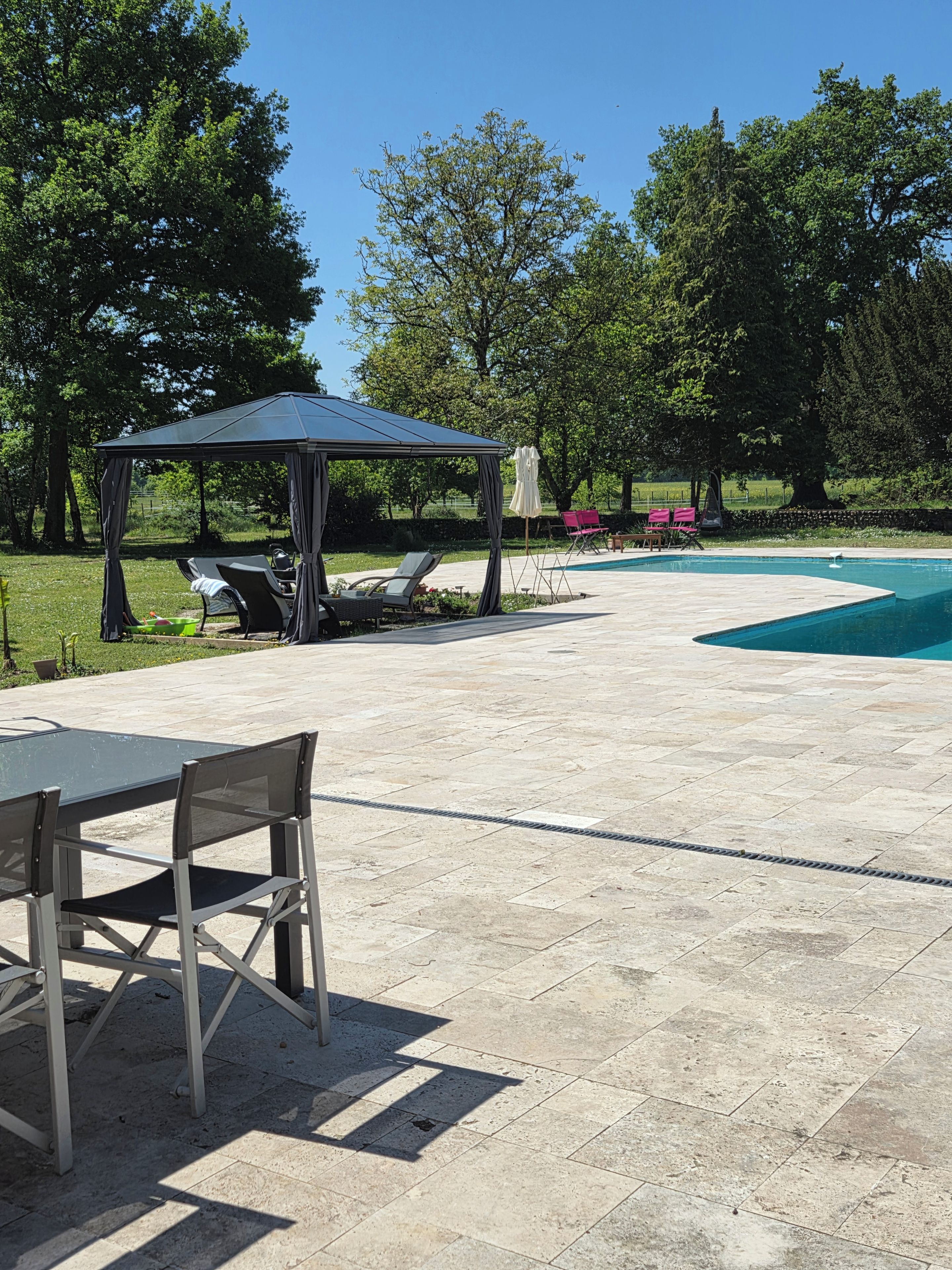 An outdoor patio with a pool, a covered seating area, and a table with chairs.