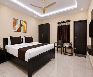 A hotel room with a bed, a desk, a chair, a wardrobe, and a ceiling fan. - Deluxe Room Sri Sai Guest House (Visakhapatnam)