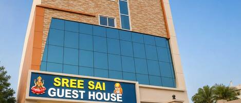 A building with a sign reading 'SREE SAI GUEST HOUSE' and a gated entrance.