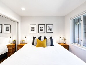 A bedroom with a large bed, bedside tables, a wardrobe, and framed pictures on the wall. - Main Village Condo | Walk to Lifts | Free Parking (Whistler)