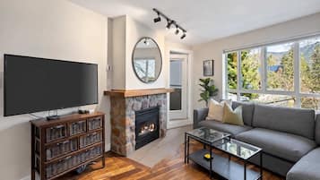 A living room with a fireplace, a television, a sofa, and a large window.