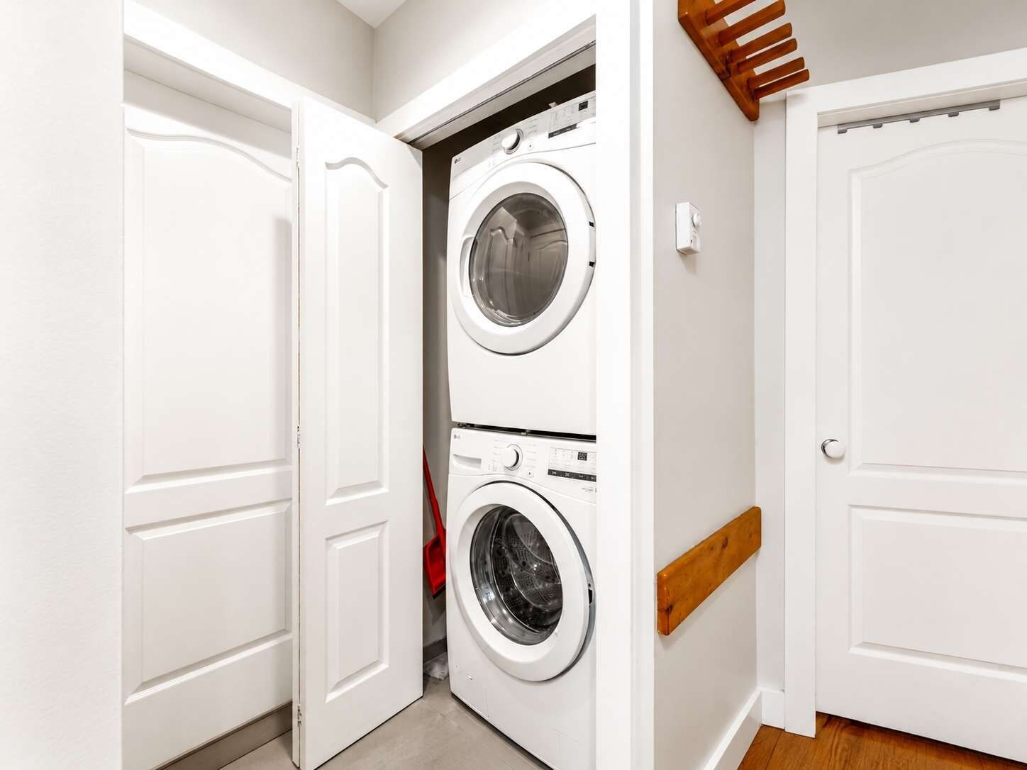 Una sala de lavandería con dos lavadoras apiladas, una cesta de ropa roja y puertas blancas.