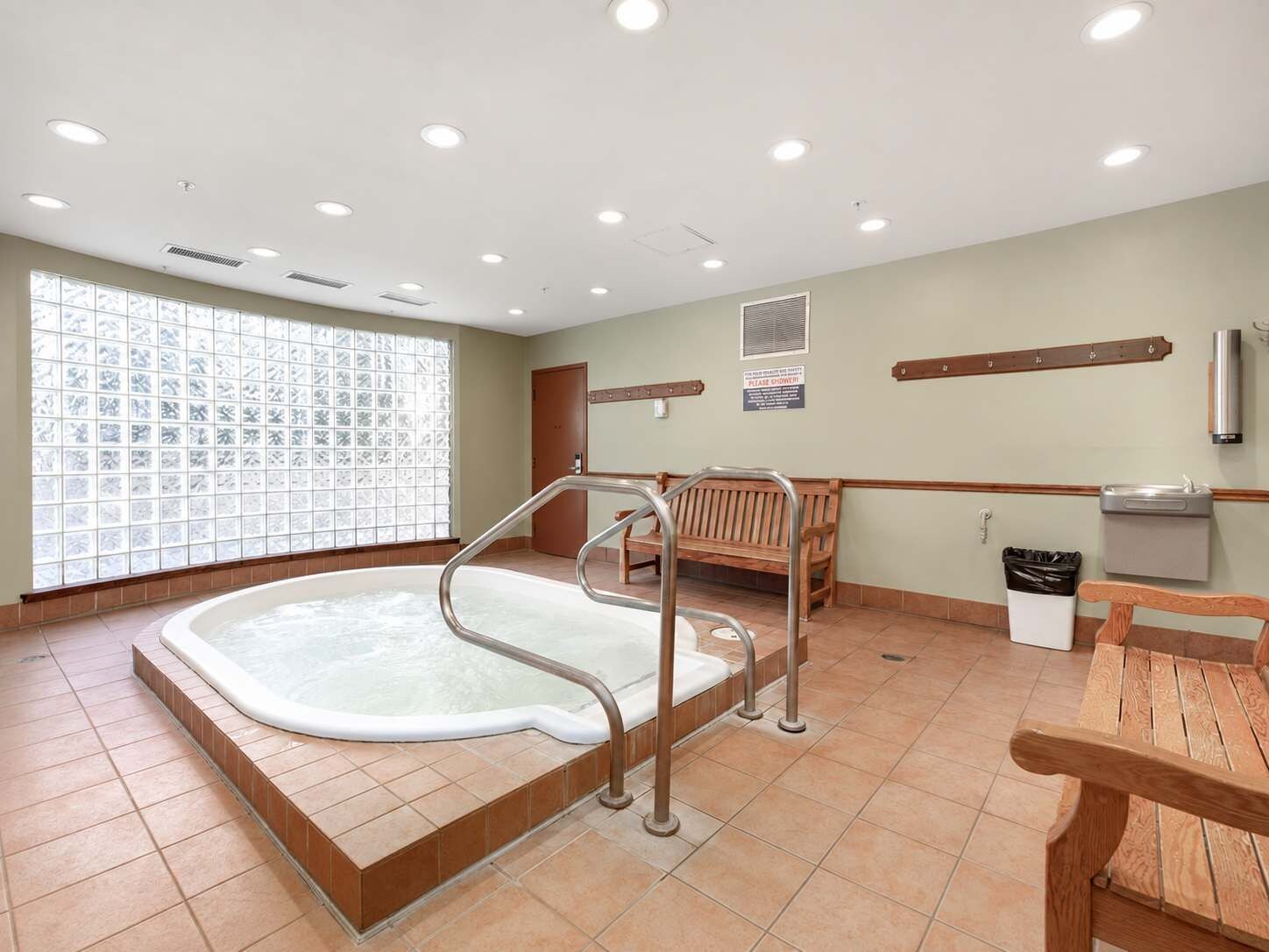 Ein Zimmer mit Whirlpool, Holzbänken, einem Mülleimer und einem Fenster mit Aussicht.