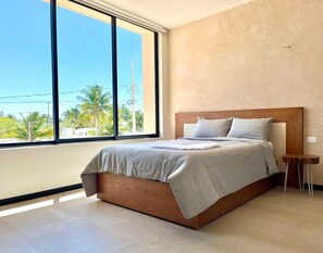 Ein Schlafzimmer mit großem Fenster, einem Bett mit Holz Kopfteil und einem kleinen Nachttisch.
