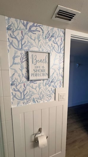 A bathroom with a wall mural of coral and sea life, a framed quote, and a toilet paper holder. - Gulf Front @ “The Coral” Breathtaking Sunsets! (Indian Shores)