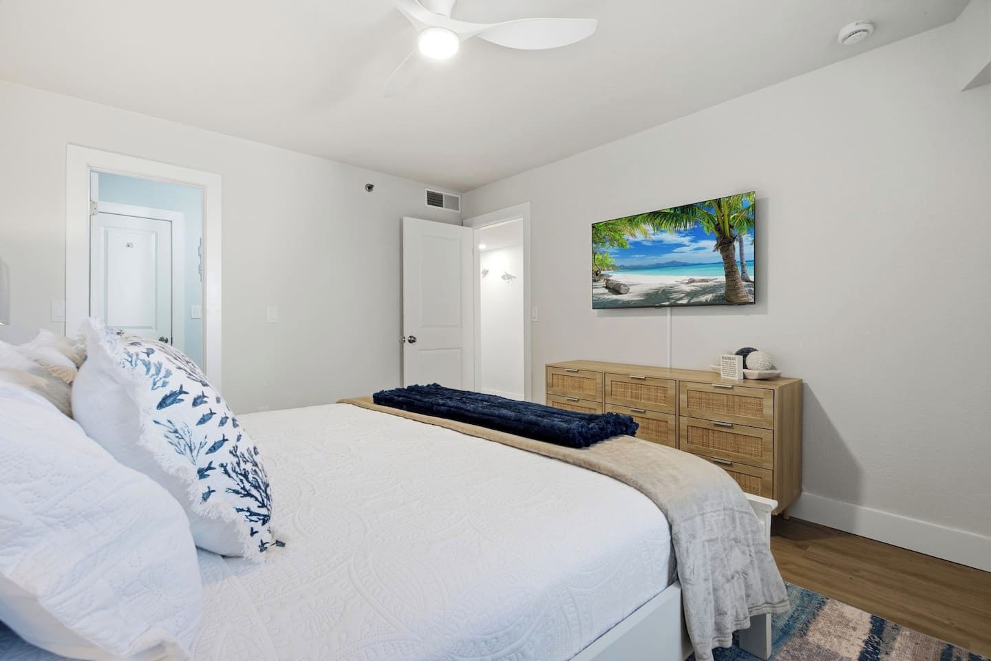 A bedroom with a bed, a dresser, a painting, and a ceiling fan.