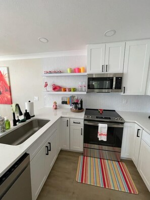 A modern kitchen with white cabinetry, a stainless steel stove, and a microwave. - Waterfront Bungalow Getaway | Sleeps 12 (Madeira Beach)