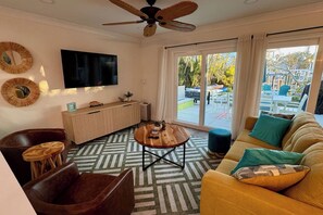 A living room with a sofa, armchair, coffee table, TV, and a ceiling fan. - Waterfront Bungalow Getaway | Sleeps 12 (Madeira Beach)