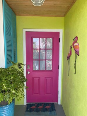 A vibrant front door with a pink color, a potted plant to the left, and two flamingo decorations on the wall. - Waterfront Bungalow Getaway | Sleeps 12 (Madeira Beach)